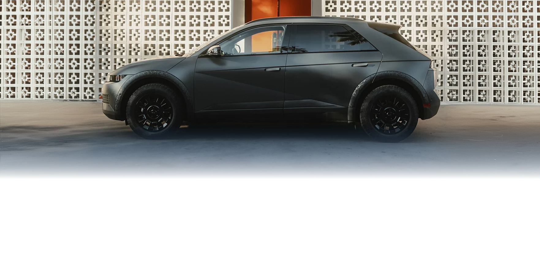 A matte black IONIQ 5 XRT in profile in front of a white breeze-block wall