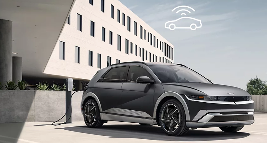A silver IONIQ 5 charging outside a modern office building with a Wi-Fi signal icon above it