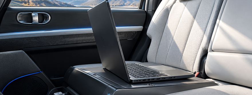 An open laptop charging on the rear seat of an IONIQ 5 with a light gray interior