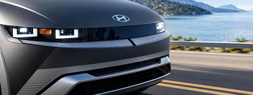 Close-up of the front of a dark IONIQ 5 driving along a coastal road