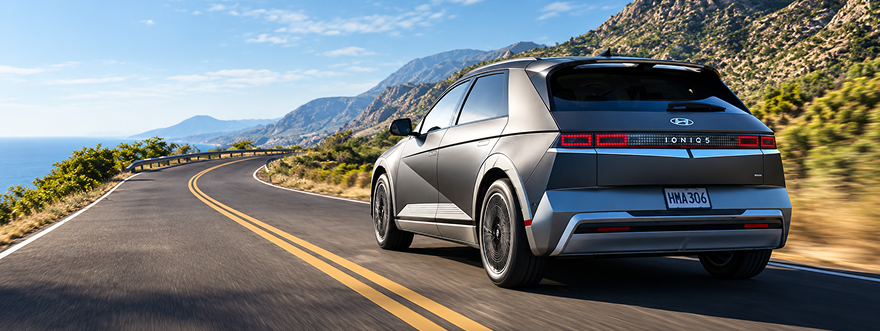 Rear view of a silver IONIQ 5 driving a winding road above the ocean