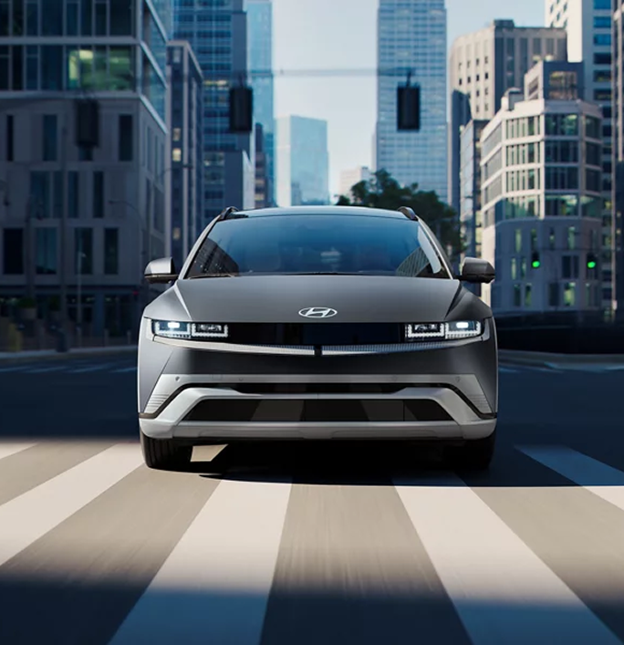 A dark IONIQ 5 seen head-on crossing a city intersection