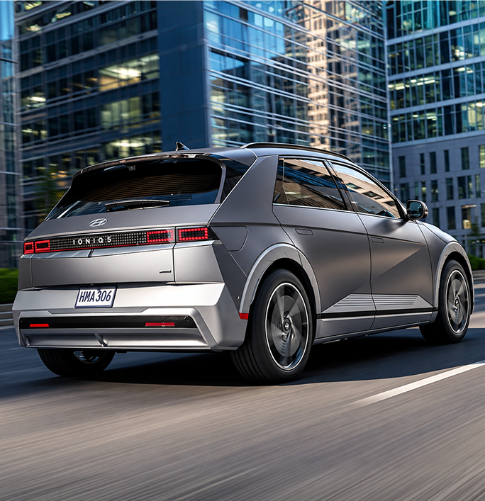 Rear three-quarter view of a silver IONIQ 5 driving past city towers