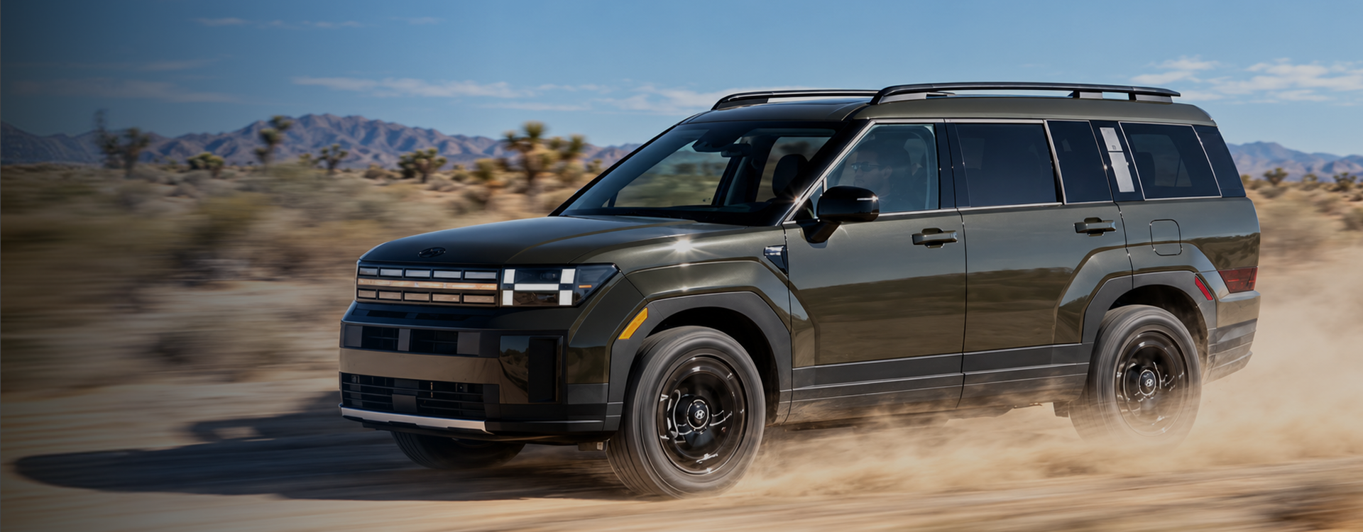 A dark green 2027 Hyundai SANTA FE driving through the desert and kicking up dust