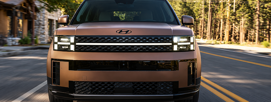Head-on view of a copper SANTA FE on a forest road showing its H-shaped LED headlights
