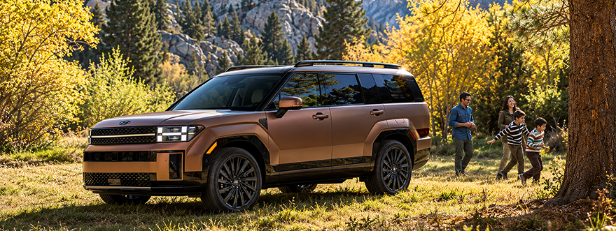 A copper SANTA FE parked in autumn woods with a family walking nearby