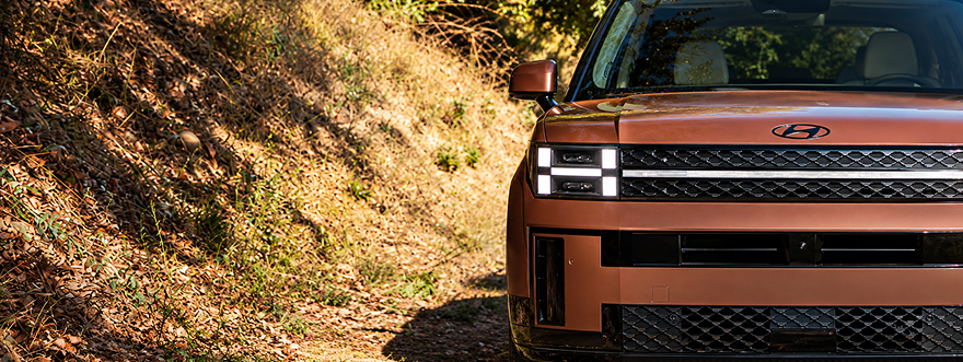 Head-on view of a copper SANTA FE Hybrid on a hillside showing its H-shaped LED headlights
