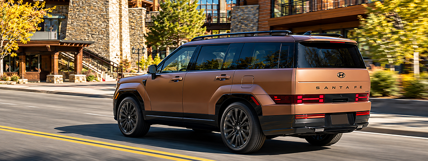 A copper SANTA FE Hybrid driving past a mountain lodge