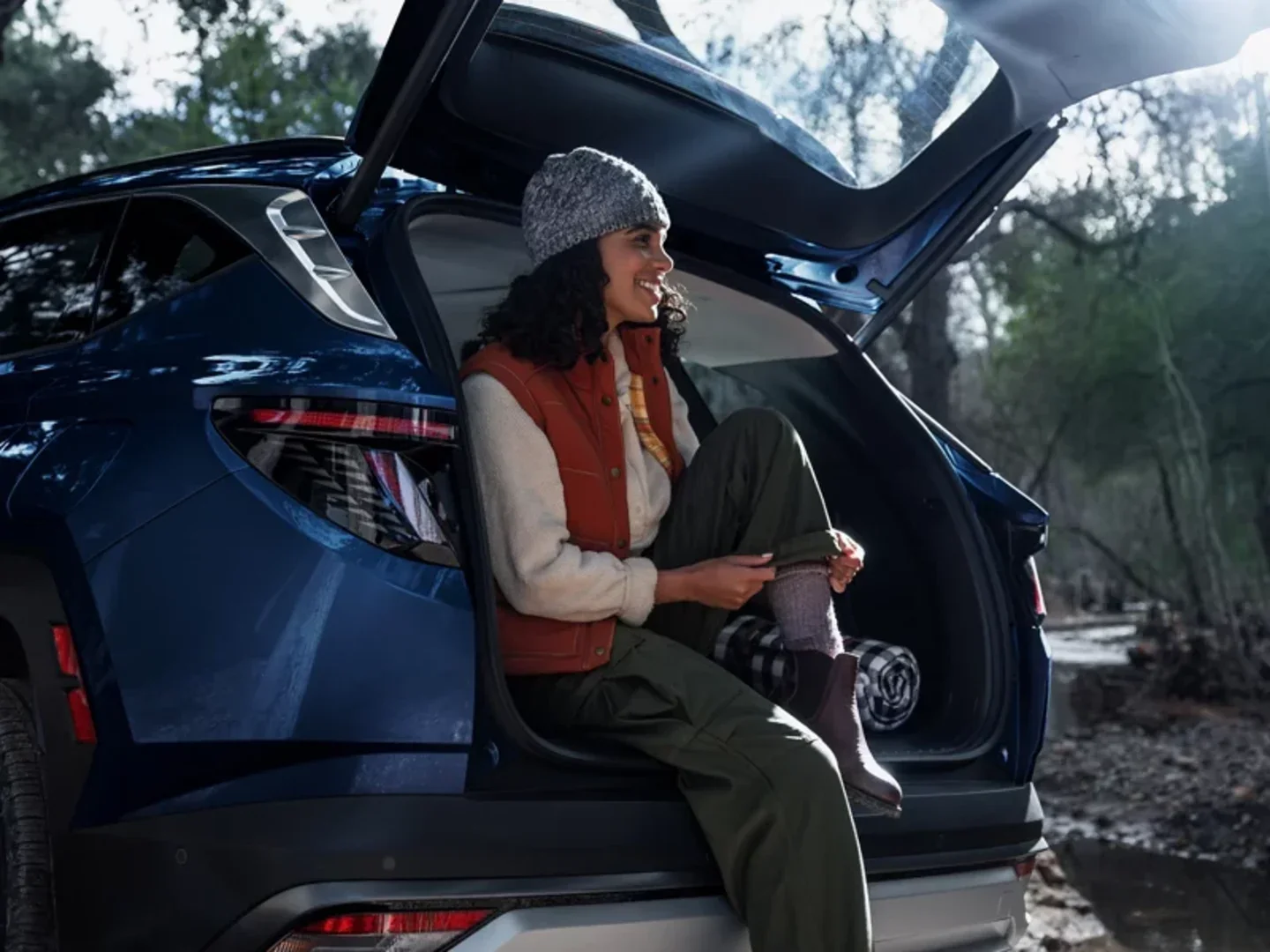 Owner sitting in the open rear tailgate of a blue Hyundai Tucson at a wooded trailhead, a trim of the SUV sold at Dalton Hyundai National City