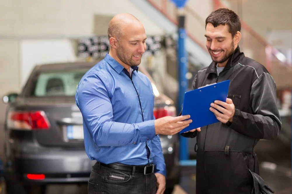 A Hyundai service advisor going over paperwork with a customer beside a car.