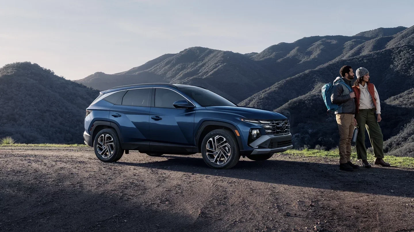 A blue Hyundai Tucson Hybrid parked in the hills beside a couple.