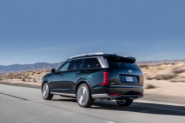 A dark blue Hyundai Palisade driving away from the camera on an open desert road