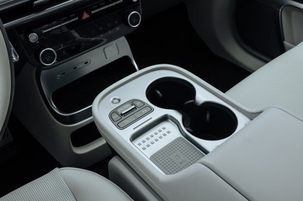 Close-up of the IONIQ 9 front center console showing cupholders and a wireless charging pad