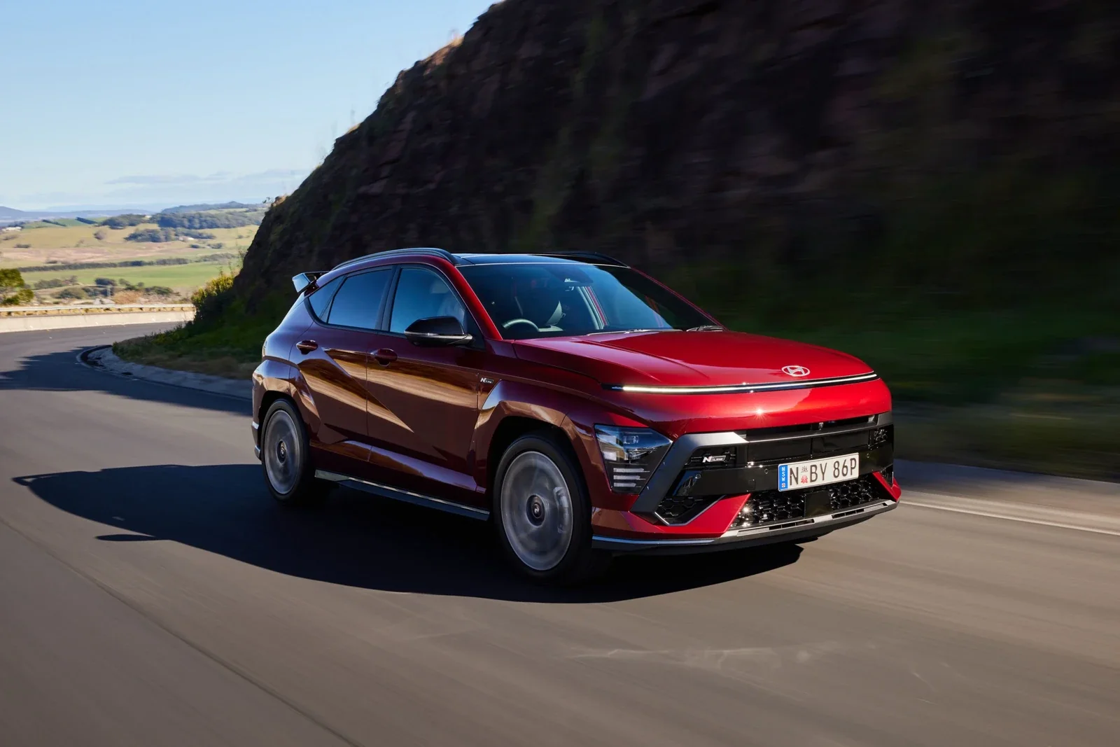 A red Hyundai Kona on a coastal road, sold at Dalton Hyundai National City